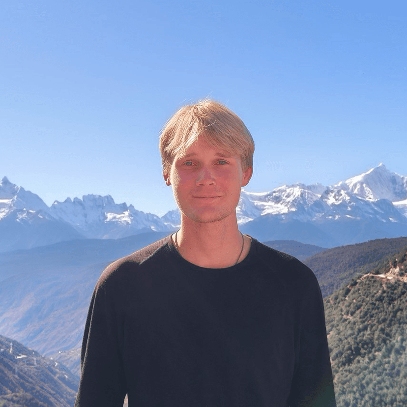 A friendly tech expert in a black sweater standing against a backdrop of snow-capped mountains on a bright, sunny day. The image conveys approachability and trustworthiness.